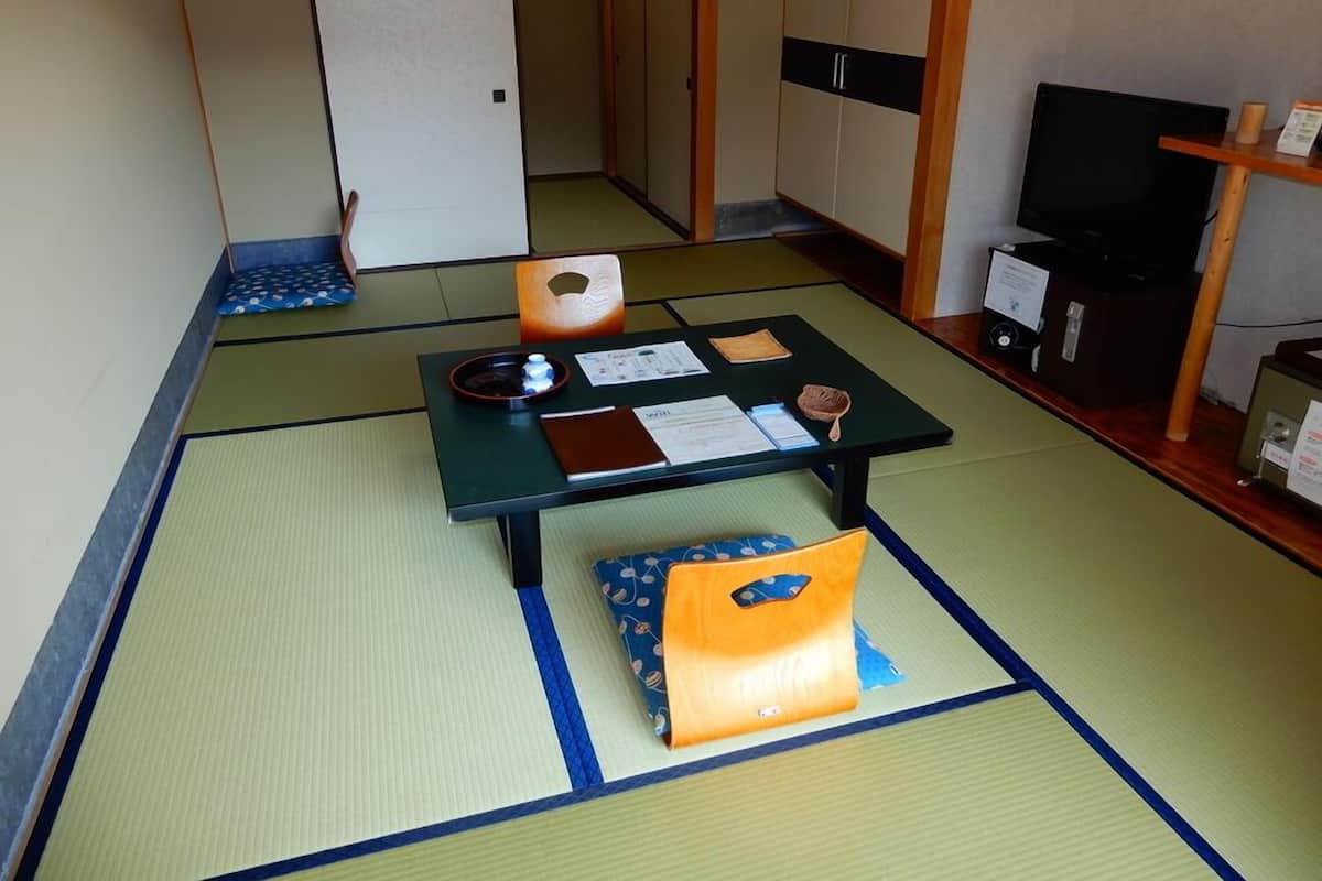 A tatami mat room with a low table, a cushion, and a television on a stand.