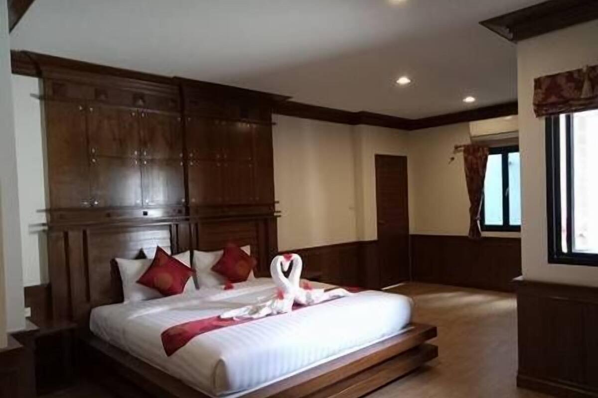 Une chambre avec un grand lit, une tête de lit en bois et une fenêtre avec des rideaux.