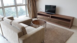 A modern living room with a beige sofa, a coffee table, and a TV on a wooden stand. - Regalia Studio 109 Suites (Kuala Lumpur)