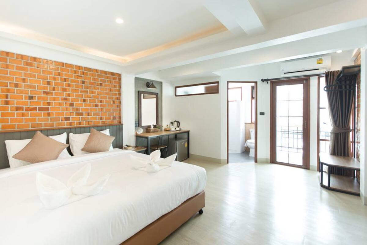 A hotel room with a large bed, a desk, a mirror, and a sliding door leading to a balcony.