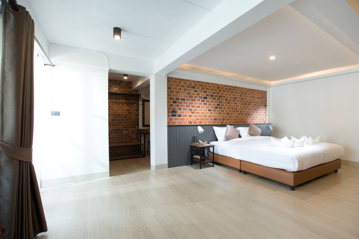 A modern bedroom with a brick accent wall, a large bed, and a small bedside table with a lamp.
