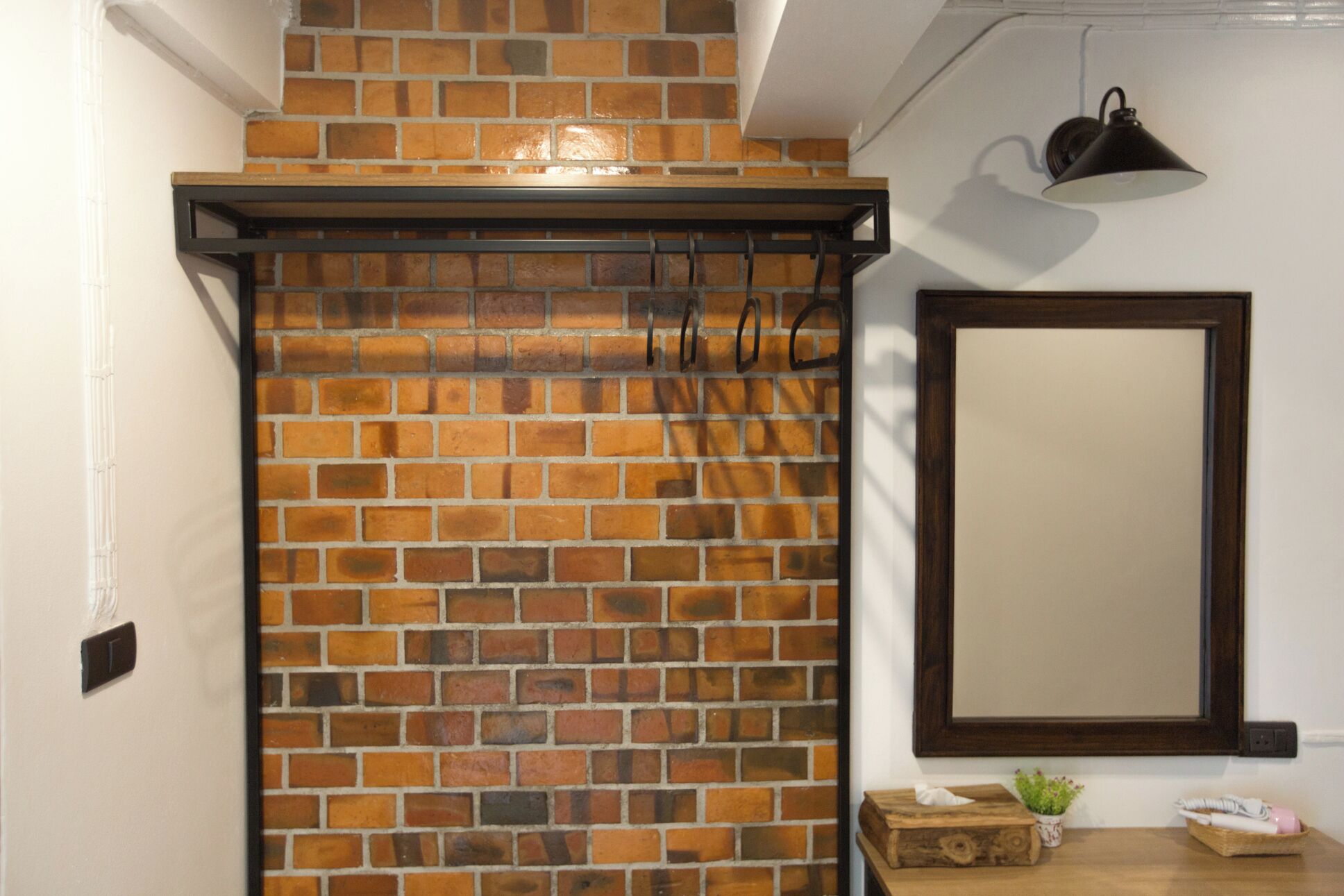 Un baño con pared de ladrillo, un banco de madera, un espejo y una lámpara.