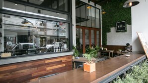 L’intérieur d’un café moderne, avec des éléments en bois, un mur vert et une vue sur la rue grâce à de grandes fenêtres.