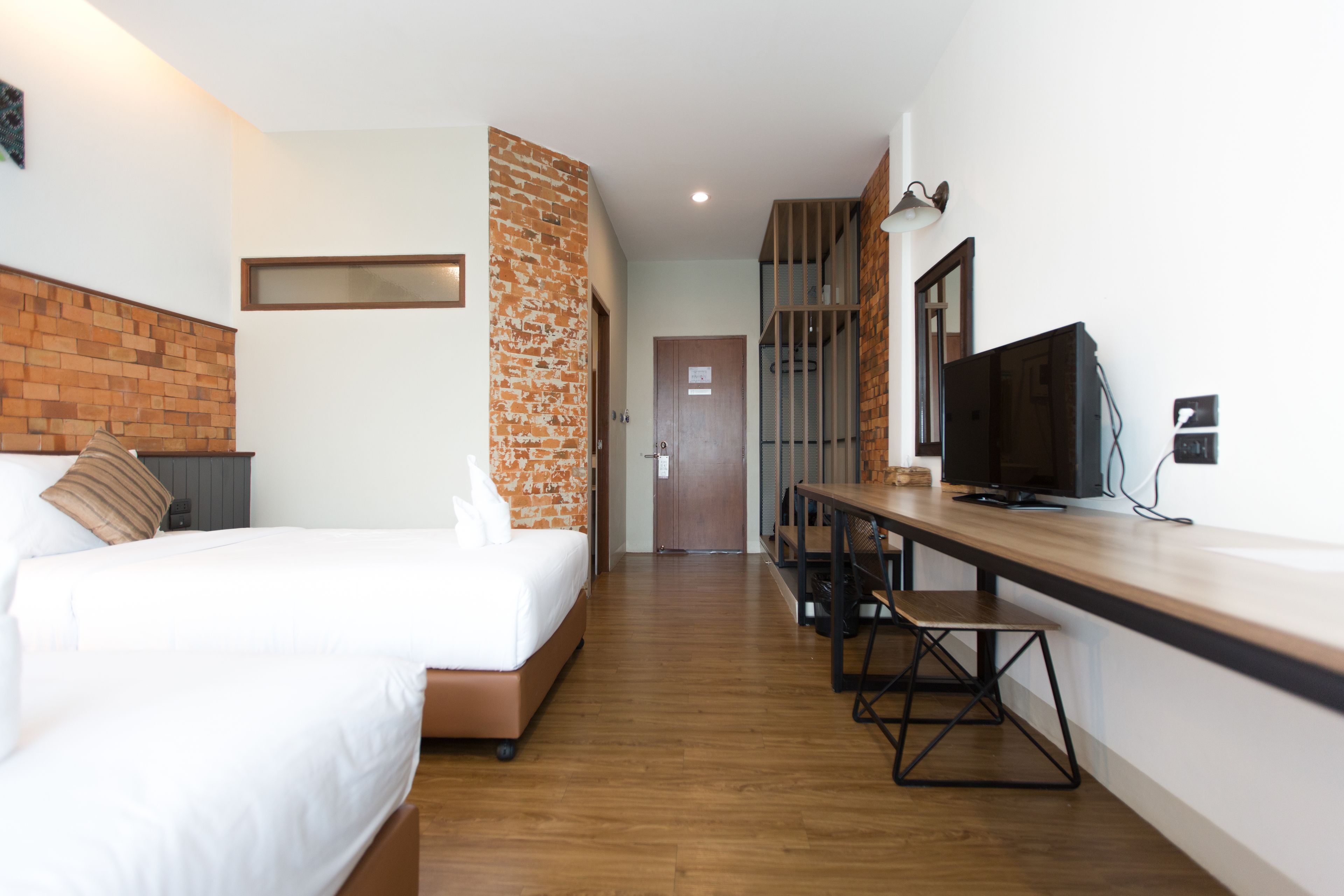 A hotel room with a bed, a desk, a television, and a brick accent wall.