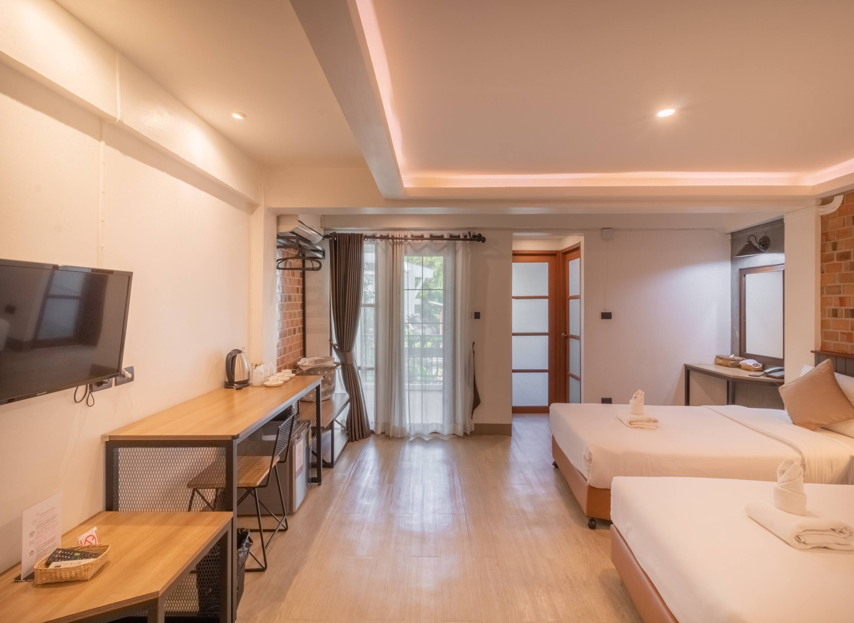 Une chambre d’hôtel équipée d’une télévision, d’un bureau avec une chaise, de deux lits, d’une petite table et d’une fenêtre avec des rideaux.