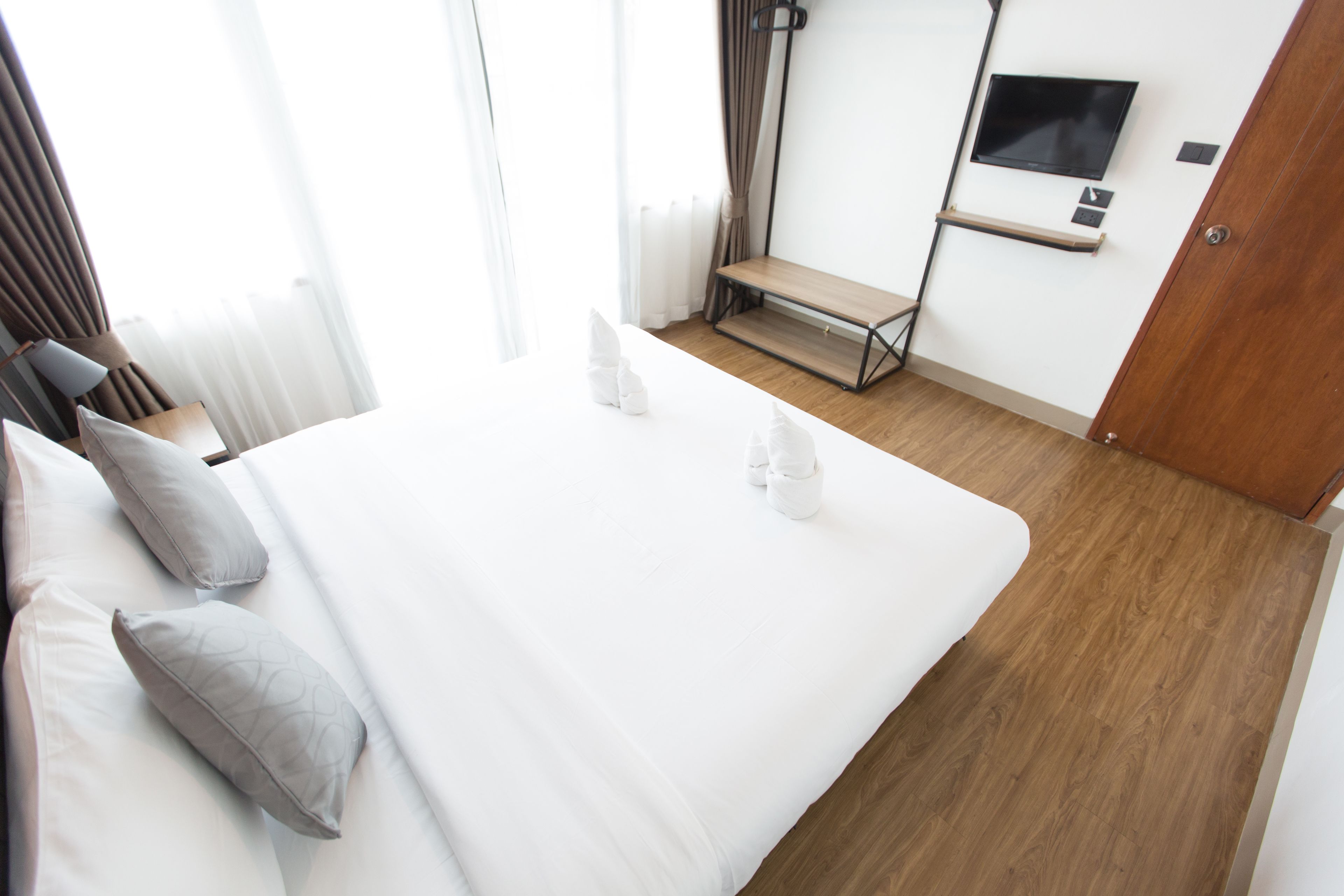 A hotel room with a large bed, a TV mounted on the wall, and a wooden floor.