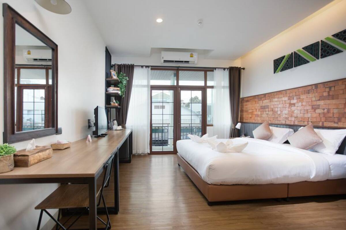 A modern hotel room with a large bed, a wooden desk, a TV, and a balcony with a view.