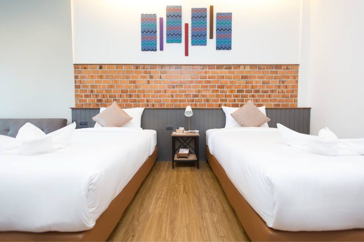 A hotel room with two beds, a brick accent wall, and a small bedside table with a lamp.