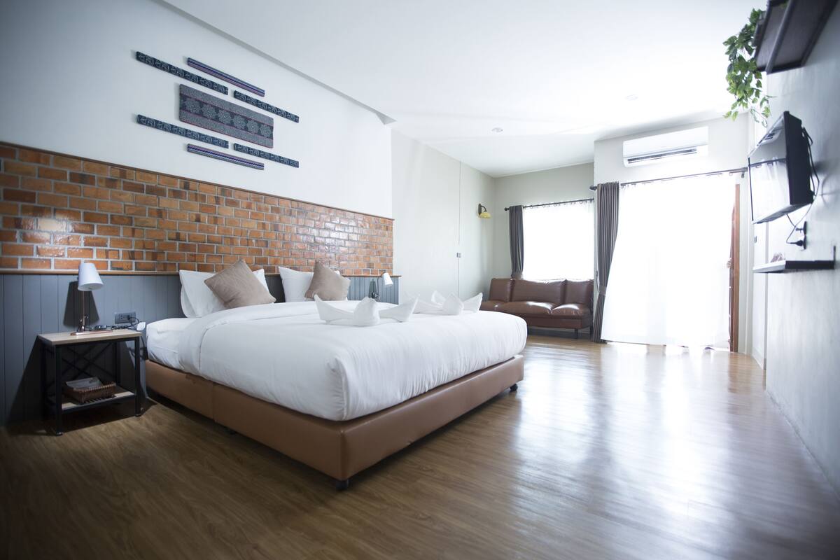 A modern hotel room with a large bed, a nightstand, a brick accent wall, and a view of the outdoors.
