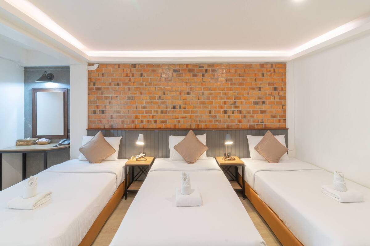 A hotel room with two single beds, a brick wall, a desk with a lamp, and a mirror.