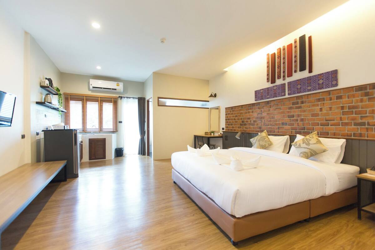 A modern hotel room with a large bed, a desk, a small kitchenette, and a brick accent wall.