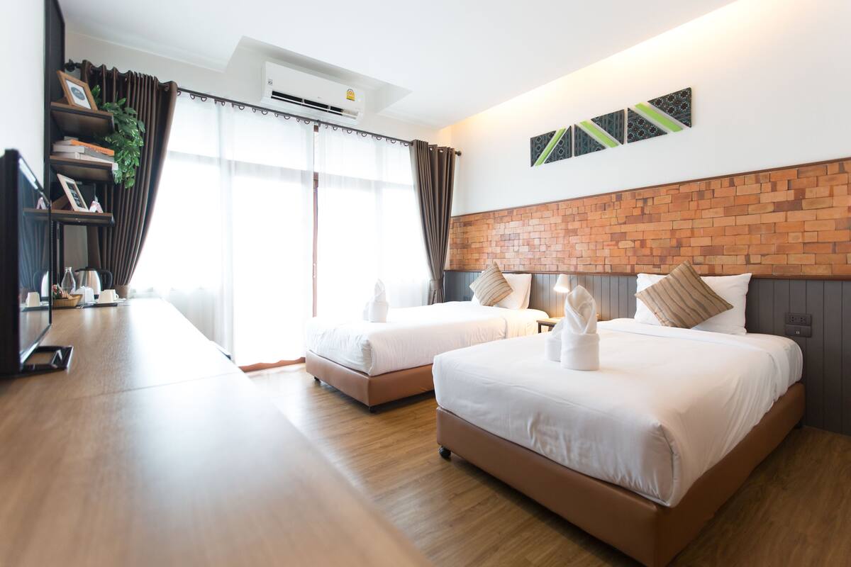 A hotel room with two beds, a wooden desk, a TV, and a brick accent wall.
