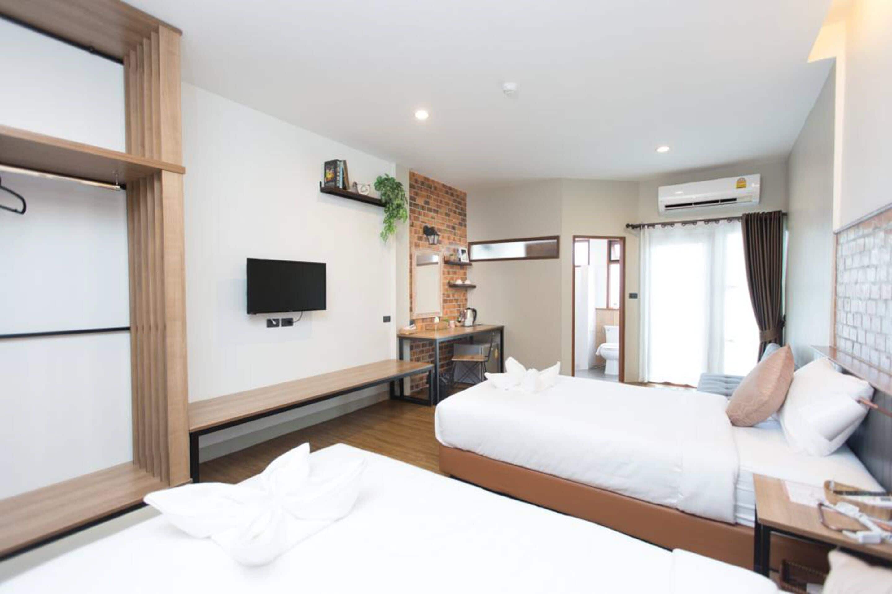 A hotel room with two beds, a desk, a TV, and an air conditioning unit.