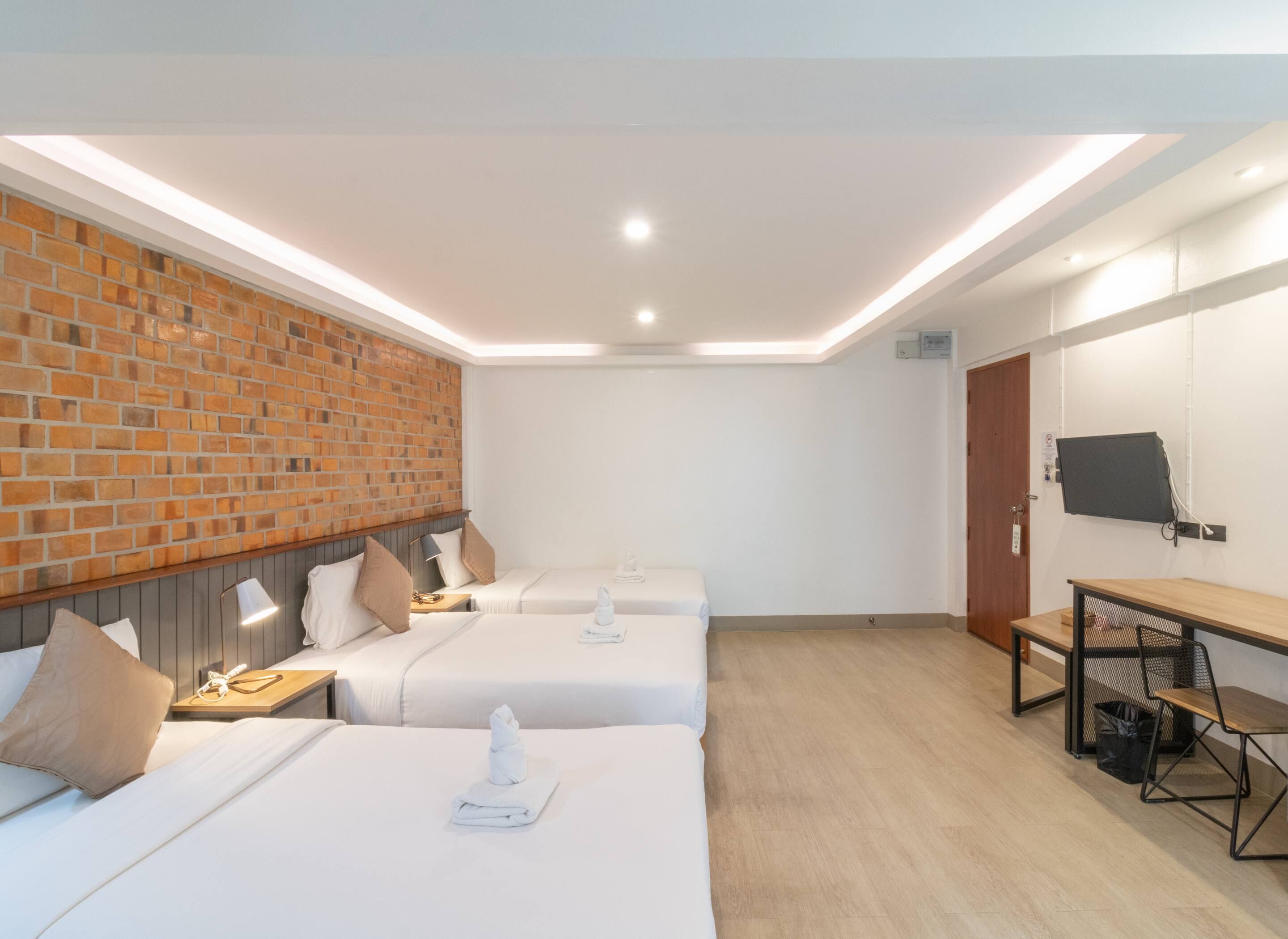 Habitación de hotel con tres camas, una pared de ladrillo, un televisor y un escritorio con una silla.