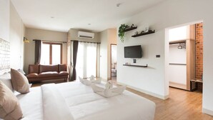 Une chambre d’hôtel avec un grand lit, un téléviseur fixé au mur, un canapé et un mur en briques.