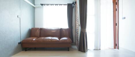 Un salón amplio con un sofá de cuero marrón, un ventanal con cortinas y una puerta que da al exterior.