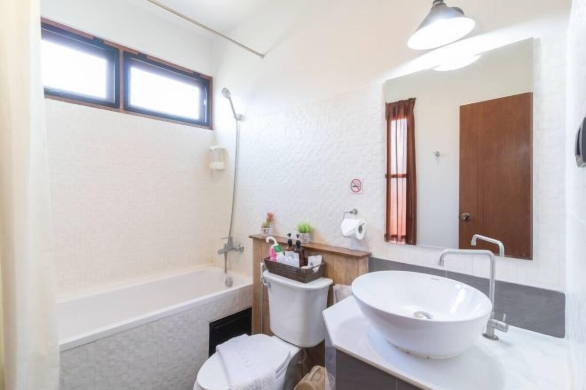 Een badkamer met een bad, toilet en wastafel. Er is een raam boven het bad en een spiegel boven de wastafel.