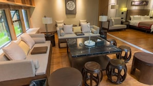 A modern living room with a sofa, coffee table, and stools. There is a dining area with a table and chairs. The room has wooden flooring and a large window. - Chengdu E Hotel (Chengdu)