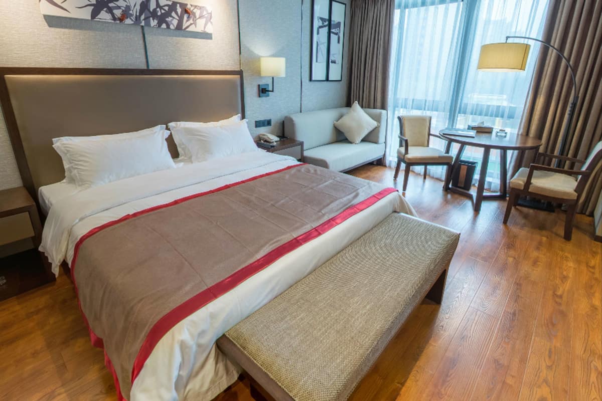 A hotel room with a large bed, a sofa, a small table, and a chair.