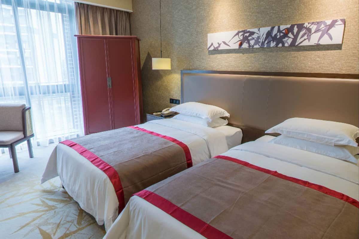 A hotel room with two beds, a desk, a chair, and a large window with curtains.