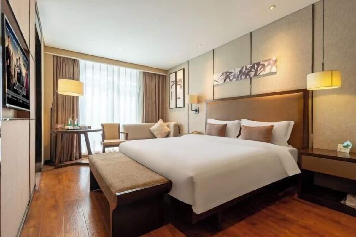 A hotel room with a large bed, a desk, a chair, and a bench.