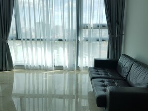 A modern living room with a black leather sofa, large windows with sheer curtains, and a reflective floor. - Kardean Intl at Vogue Suite (Kuala Lumpur)