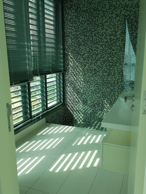 A bathroom with a large window, a tiled floor, and a white bathtub. - Kardean Intl at Vogue Suite (Kuala Lumpur)