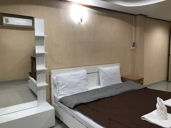 A modern bedroom with a bed, white nightstands, a built-in shelf unit, and a wall-mounted air conditioning unit.