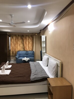 A modern hotel room with a bed, a blue sofa, a small table, and a ceiling fan. - President Apartment (Pattaya)