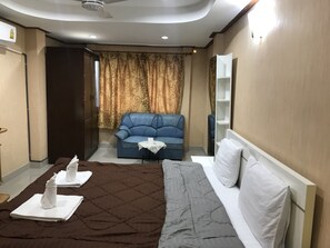 A hotel room with a bed, a blue sofa, a small table with a white cloth, and a curtain with a gold pattern. - President Apartment (Pattaya)