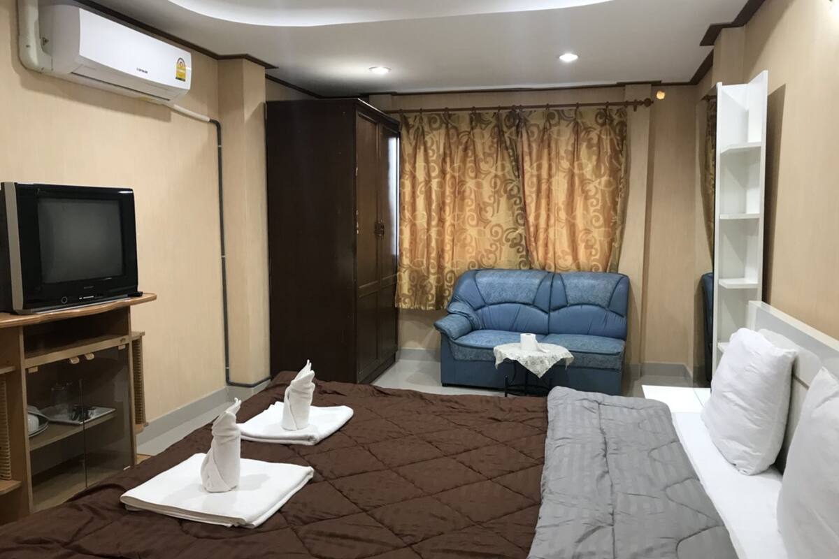 A hotel room with a bed, a television, a sofa, and a wardrobe.