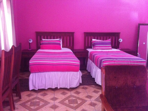 A room with two beds, each with a striped bedspread and pillows, wooden headboards, and a patterned floor. - Gomwe Guest Inn (Nata)