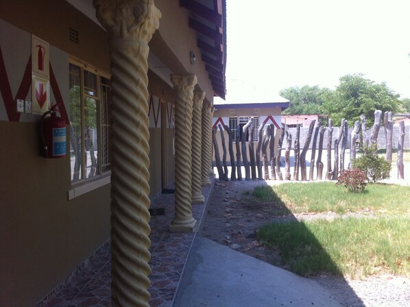 A building with a covered walkway, fire extinguisher, and a fence with wooden posts.