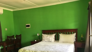 A room with a green wall, a wooden bed with floral bedding, a nightstand, a chair, and a small table with a lamp.