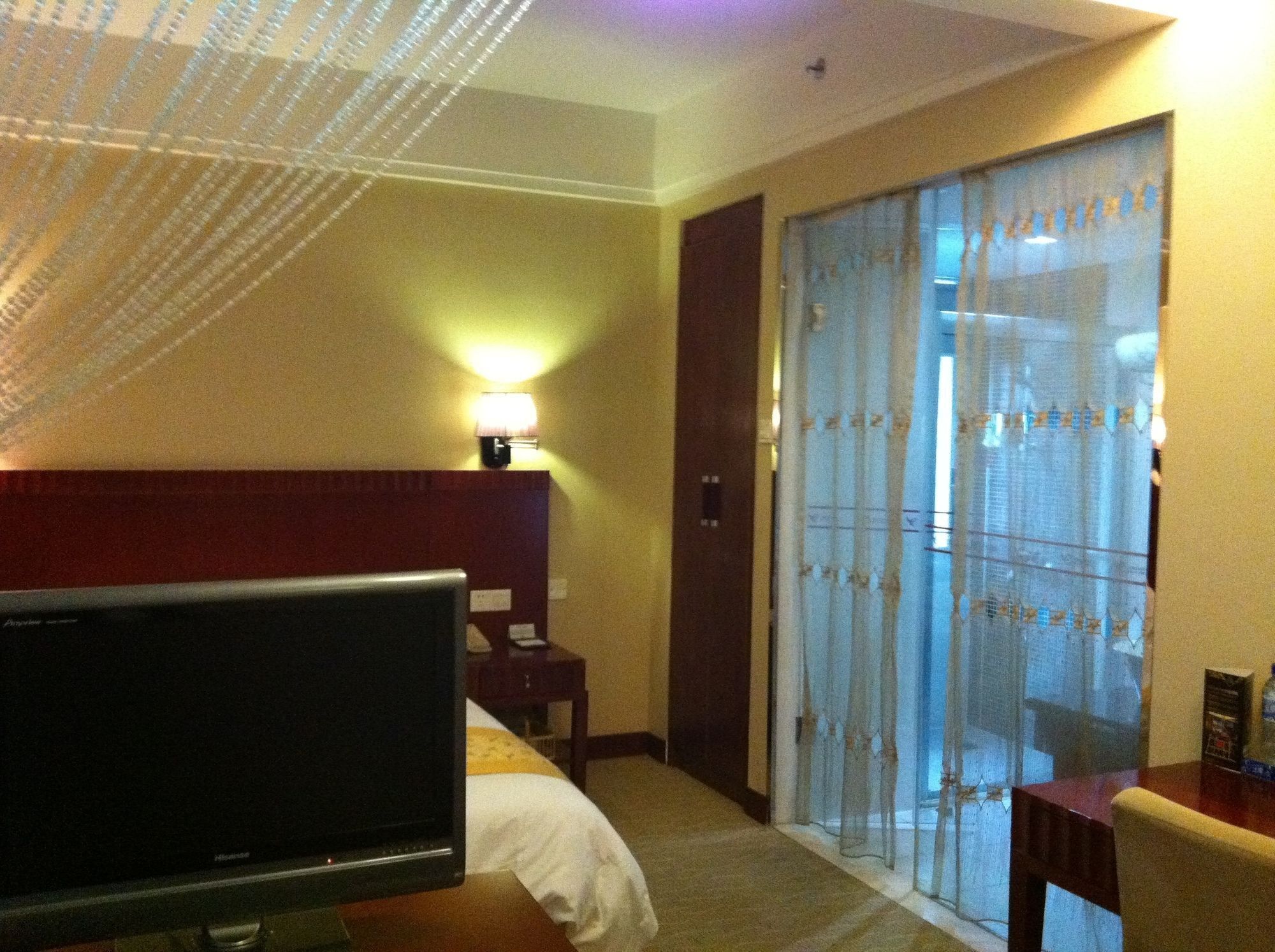Ein Hotelzimmer mit Bett, Fernseher, Schreibtisch und einer Glastür, die auf einen Balkon führt.