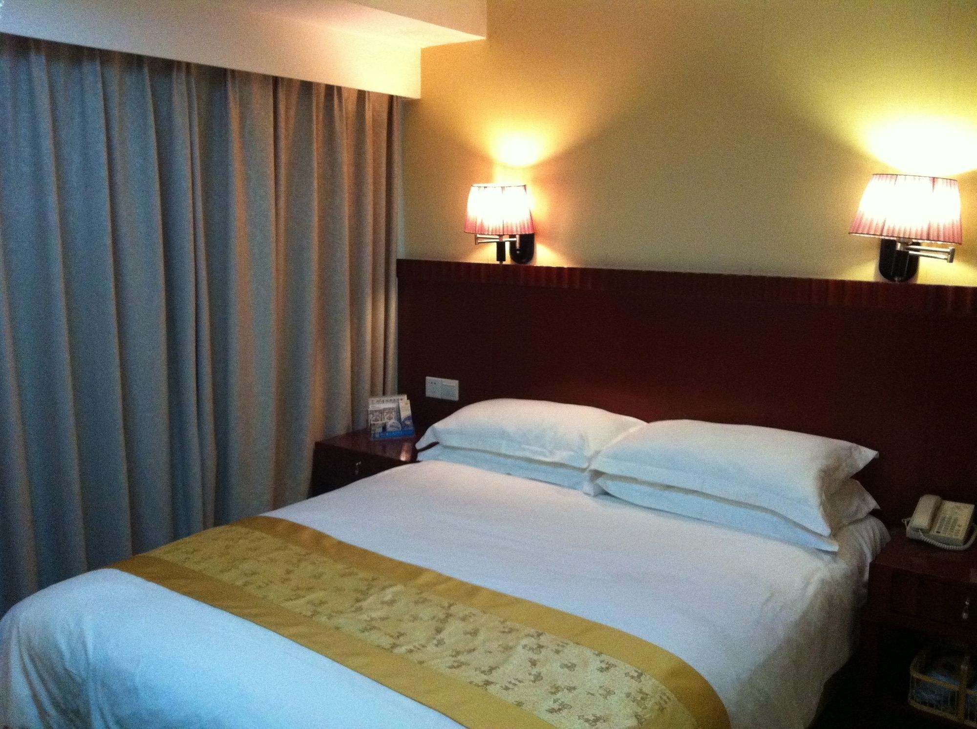 A hotel room with a bed, two bedside lamps, a telephone, and a nightstand.