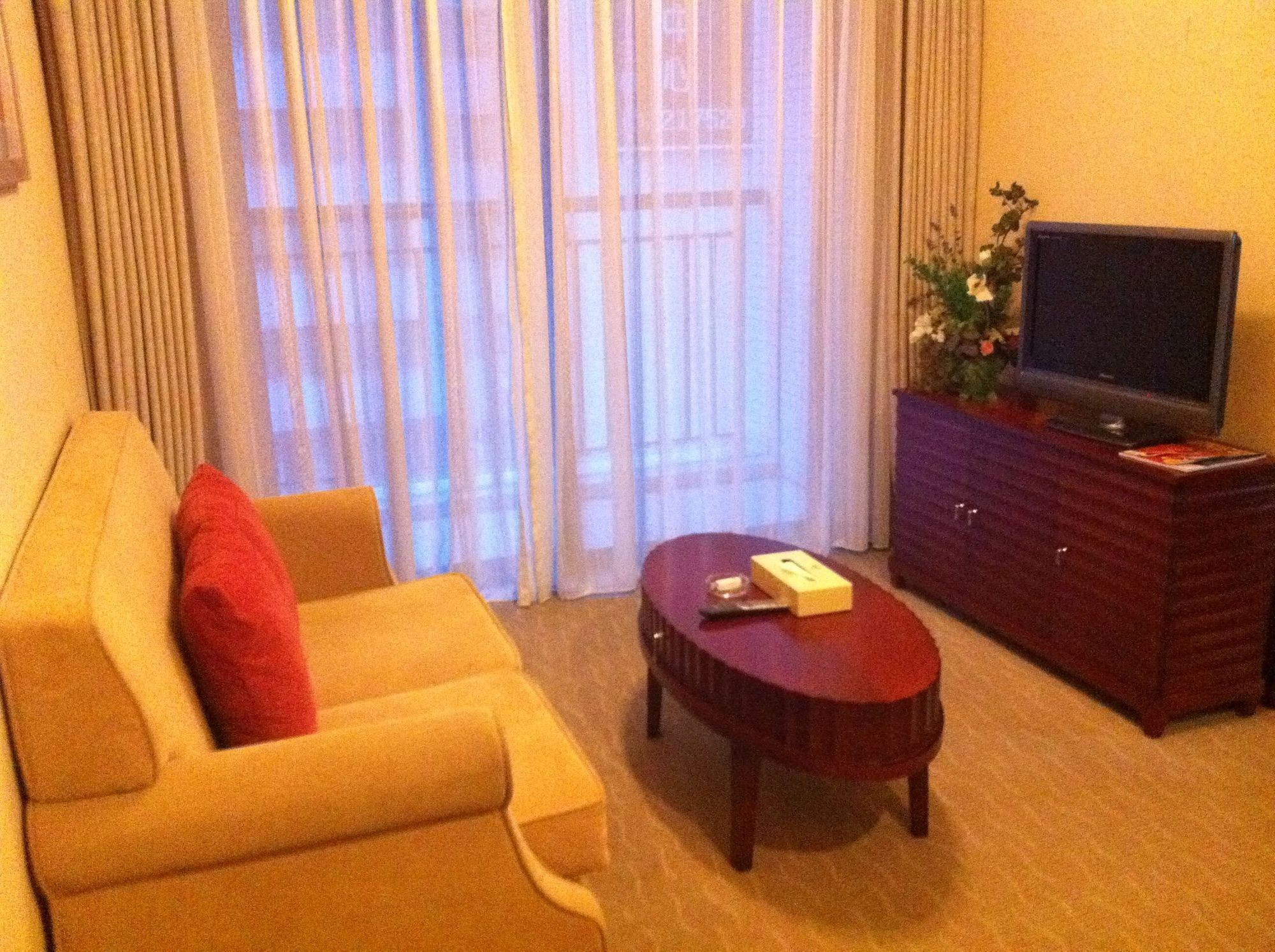Une chambre d’hôtel avec un canapé, une table basse, un téléviseur à écran plat posé sur un meuble et une fenêtre avec des rideaux.