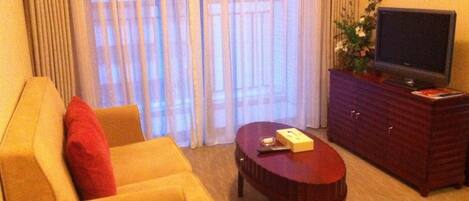 Une chambre d’hôtel avec un canapé, une table basse, un téléviseur à écran plat posé sur un meuble et une fenêtre avec des rideaux.