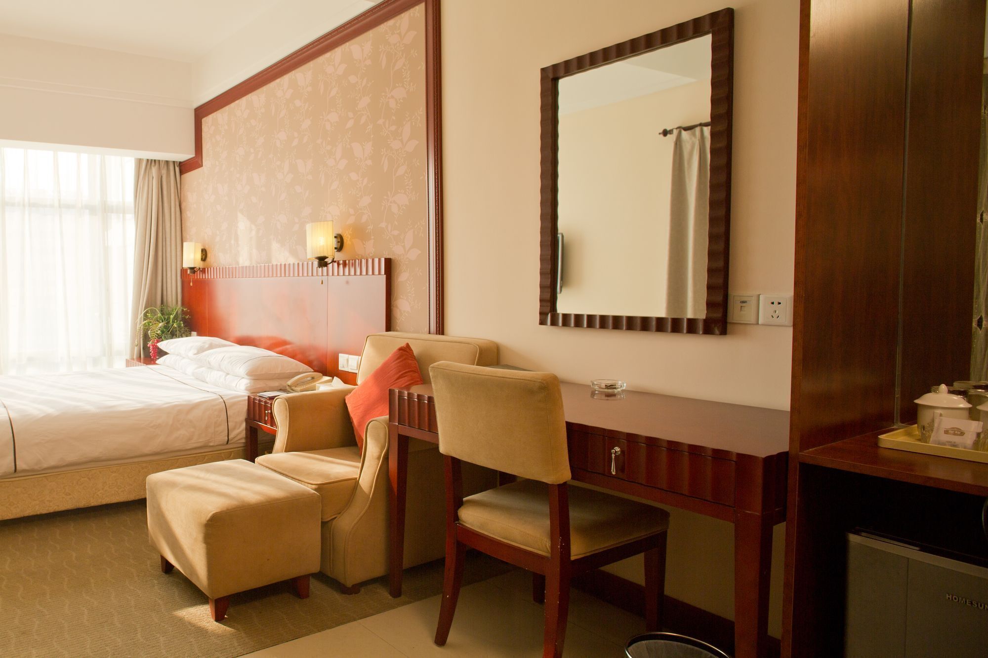 A hotel room with a bed, a desk, a chair, a mirror, and a television.