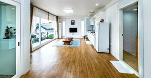 A modern kitchen with a large island, a dining area with a bench, and a view of a balcony. - Mamma House (Jeju City)
