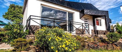 A modern house with a large glass door, a stone foundation, and a metal balcony.