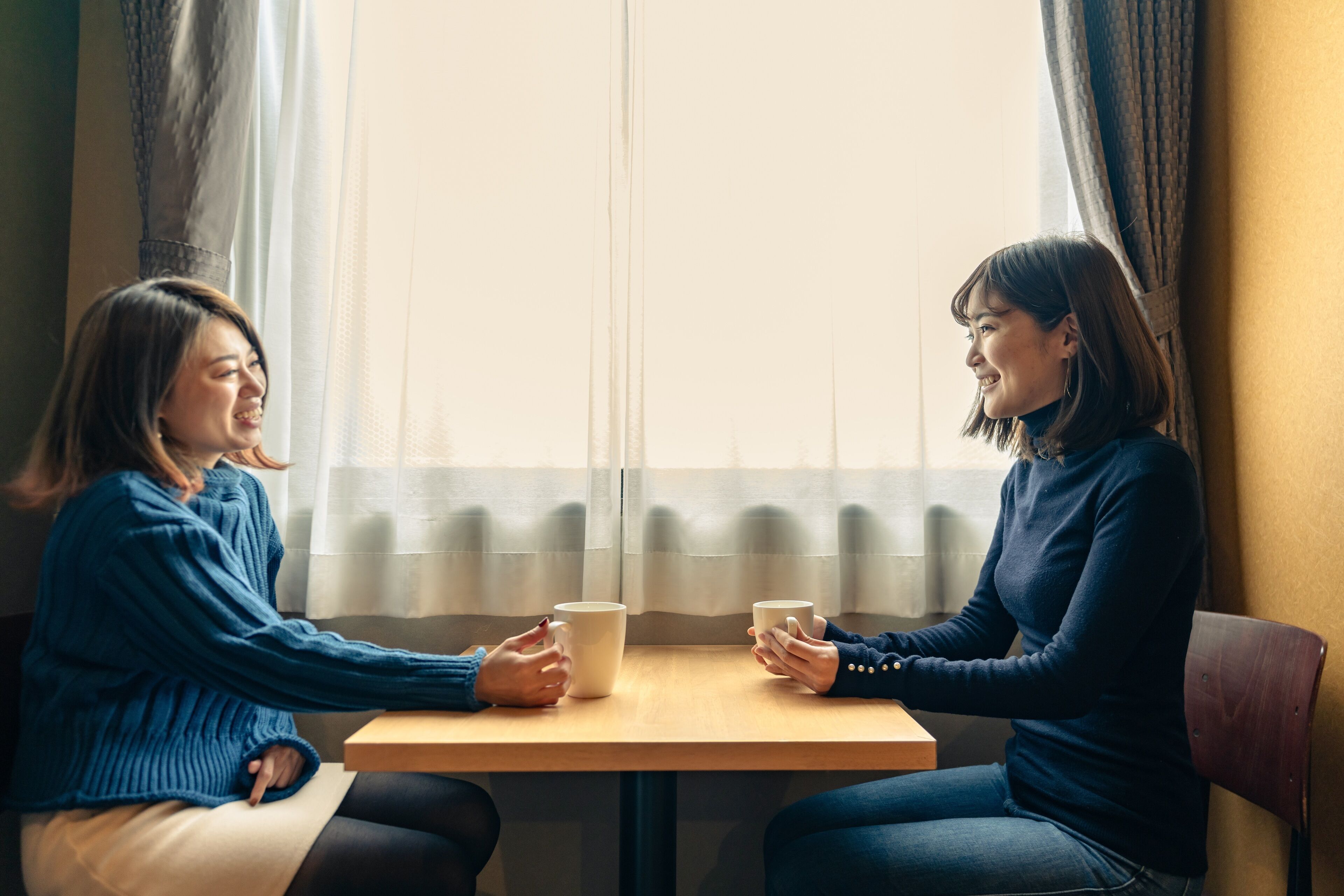 Dos personas sentadas en una mesa con una ventana al fondo.