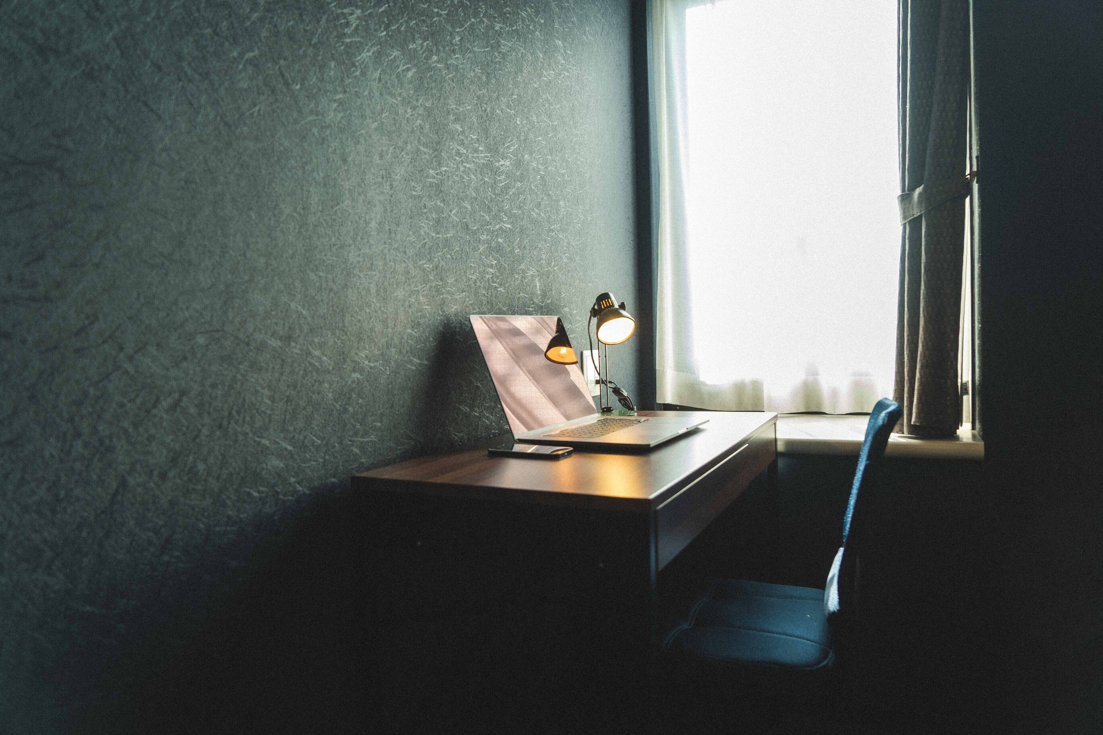 A desk with a laptop, a lamp, and a picture frame near a window with curtains.