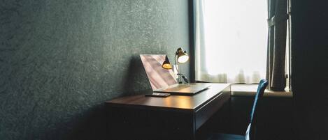 A desk with a laptop, a lamp, and a picture frame near a window with curtains.