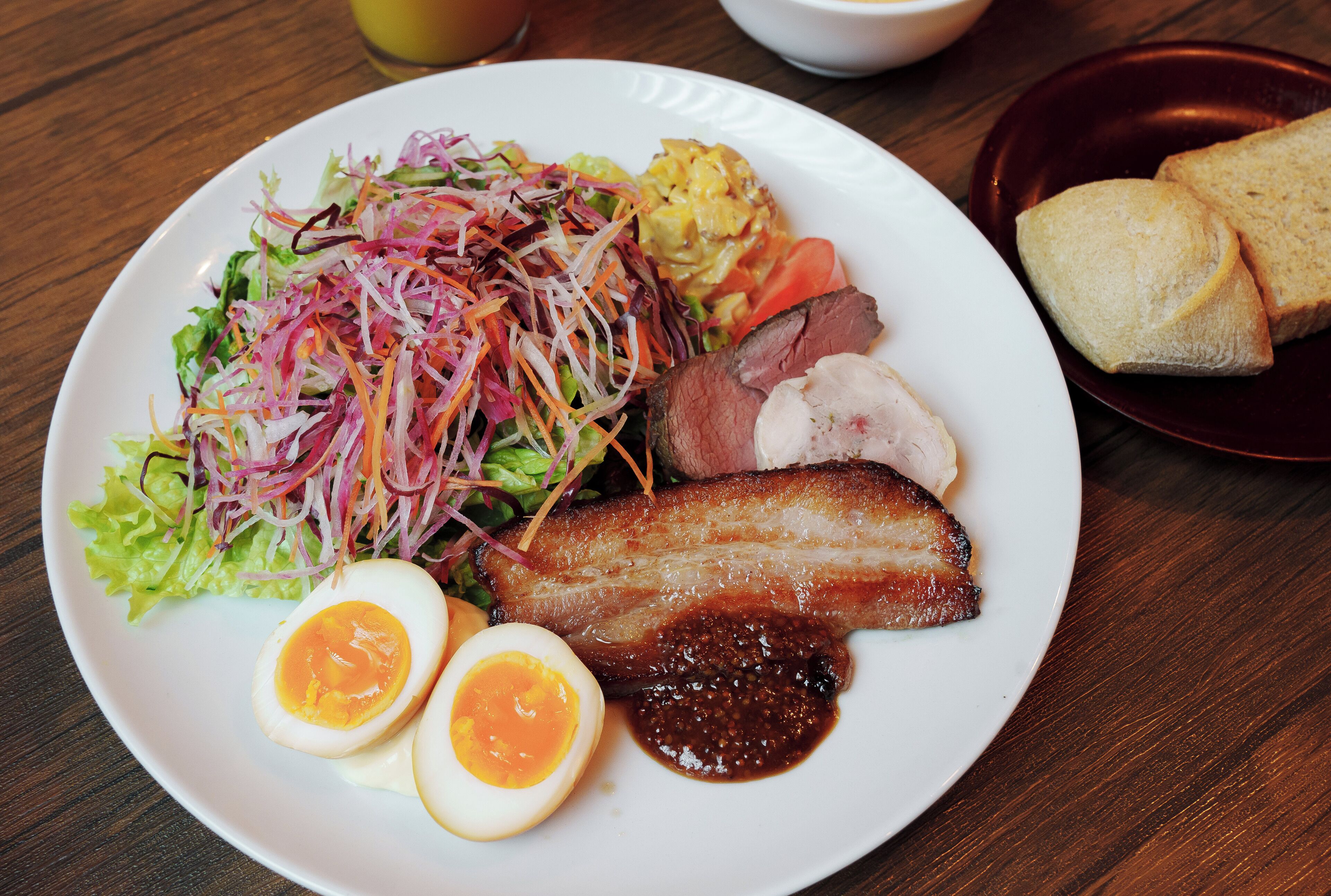 A plate with a salad, sliced meat, boiled eggs, and a side of bread.