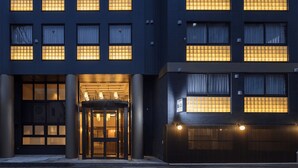 A modern building with a dark facade, multiple windows with illuminated interiors, and a revolving door at the entrance. - LINNAS Kanazawa (Kanazawa)