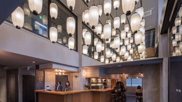 A modern hotel lobby with a wooden reception desk, multiple seating areas, and traditional lanterns hanging from the ceiling. - LINNAS Kanazawa (Kanazawa)