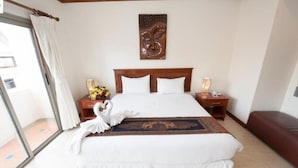 Quarto de hotel com uma cama grande, cabeceira de madeira, duas mesas de cabeceira com luminárias, um ornamento na parede e vista através de uma porta de vidro.