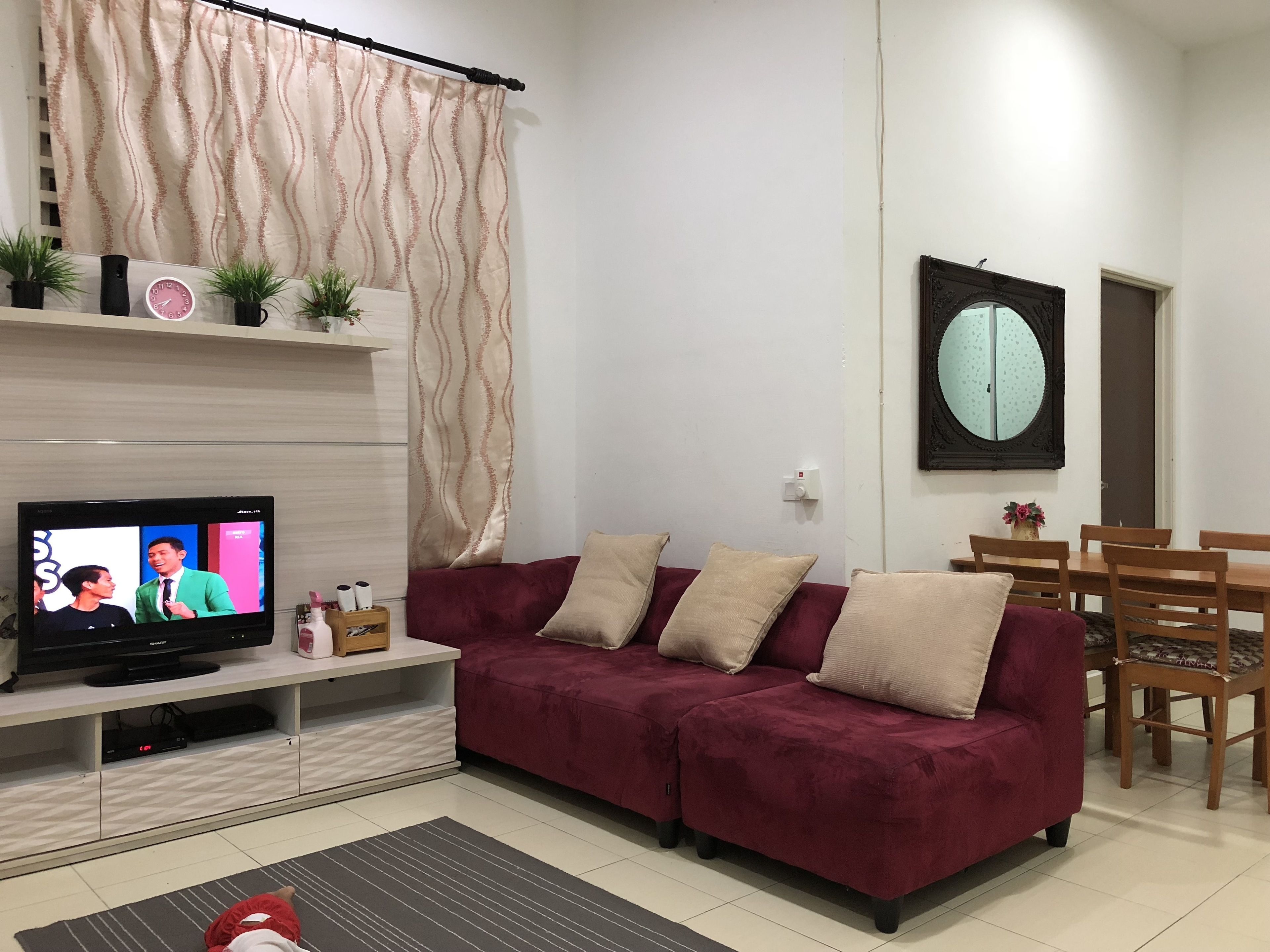 Ein Wohnzimmer mit Fernseher, einem roten Sofa, einem Holzesstisch und einem Spiegel an der Wand.