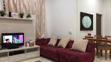 Ein Wohnzimmer mit Fernseher, einem roten Sofa, einem Holzesstisch und einem Spiegel an der Wand.